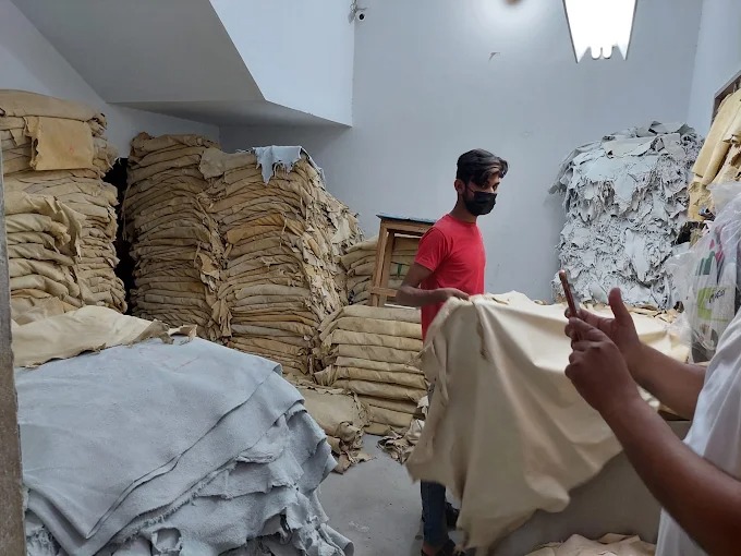 Factory worker inspecting large stacks of raw leather hides inside a garment manufacturing facility by Maswiz Industries.