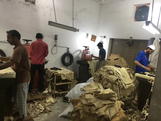 Factory workers crafting and processing leather hides at workbench machinery in the Maswiz Industries manufacturing facility.