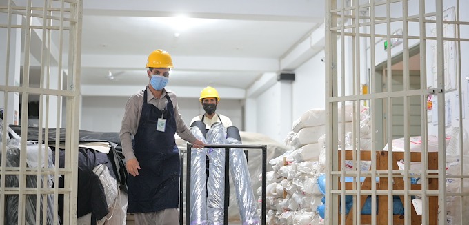 Factory workers wearing safety helmets and aprons transporting raw fabric rolls through the warehouse gate at Maswiz Industries.